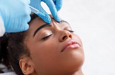 black lady with eyes closed and needle near eyebrows